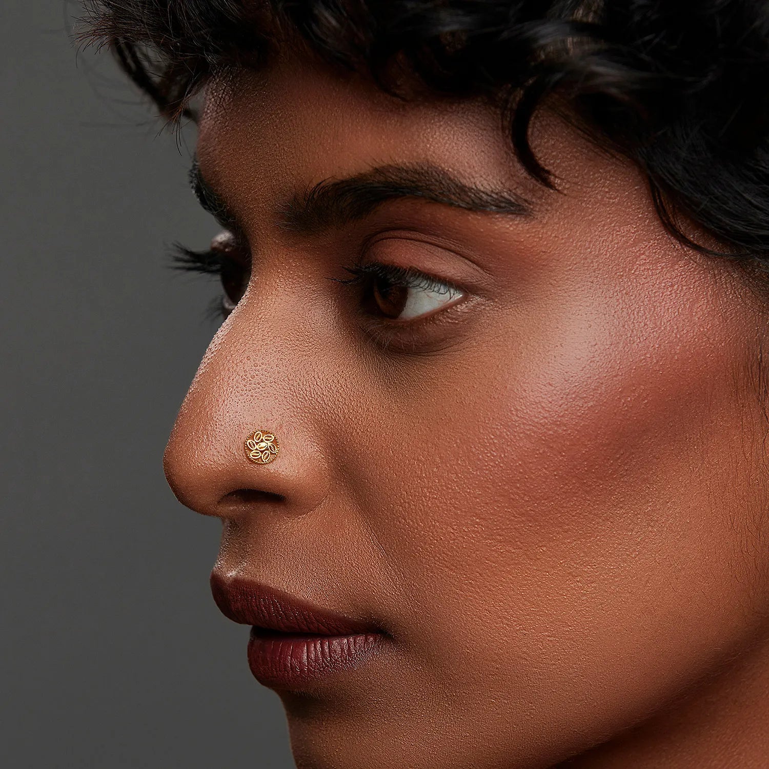 Woman wearing an elegant 18K gold nose pin showcasing its intricate round design in a side-profile view