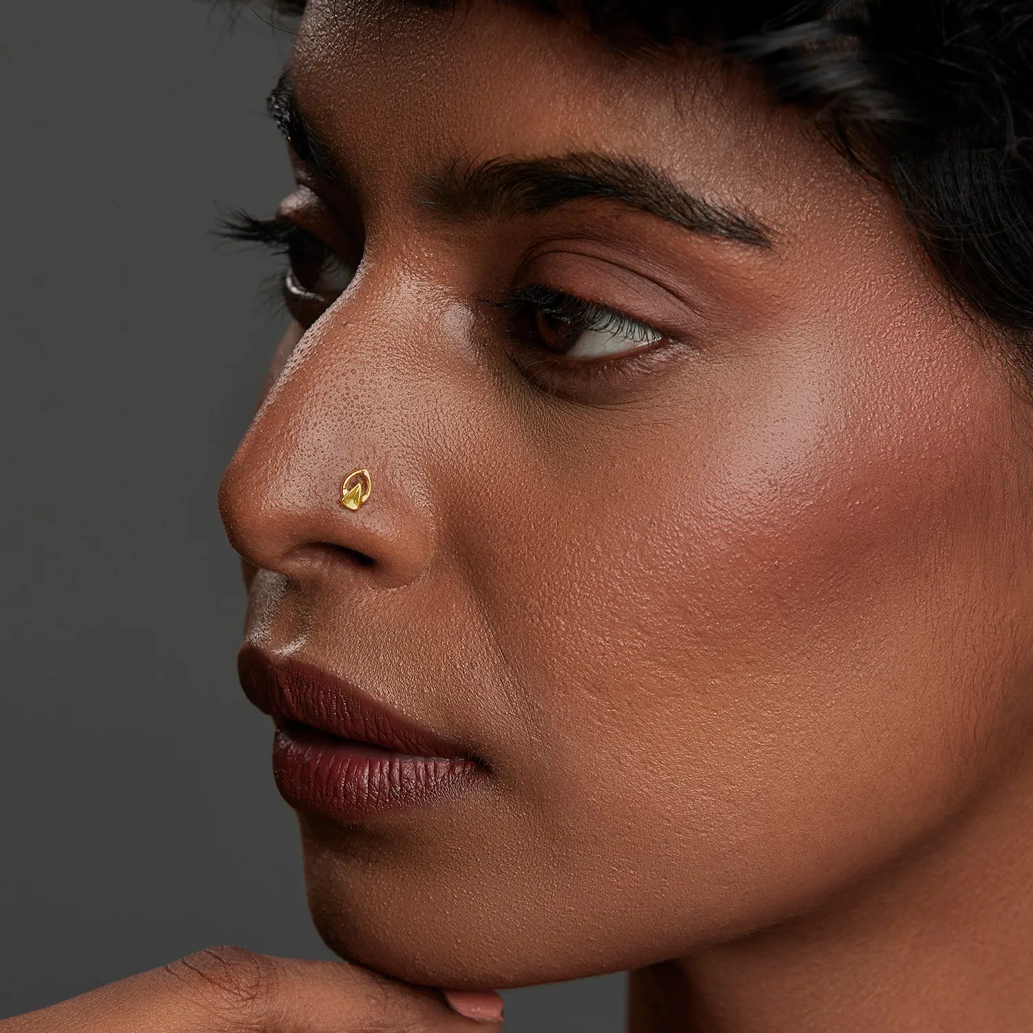 Woman wearing a minimalist 18K gold nose pin shown in side profile highlighting an elegant everyday look