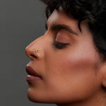 Side profile lifestyle shot of a woman wearing a round 18K gold nose pin on her nose