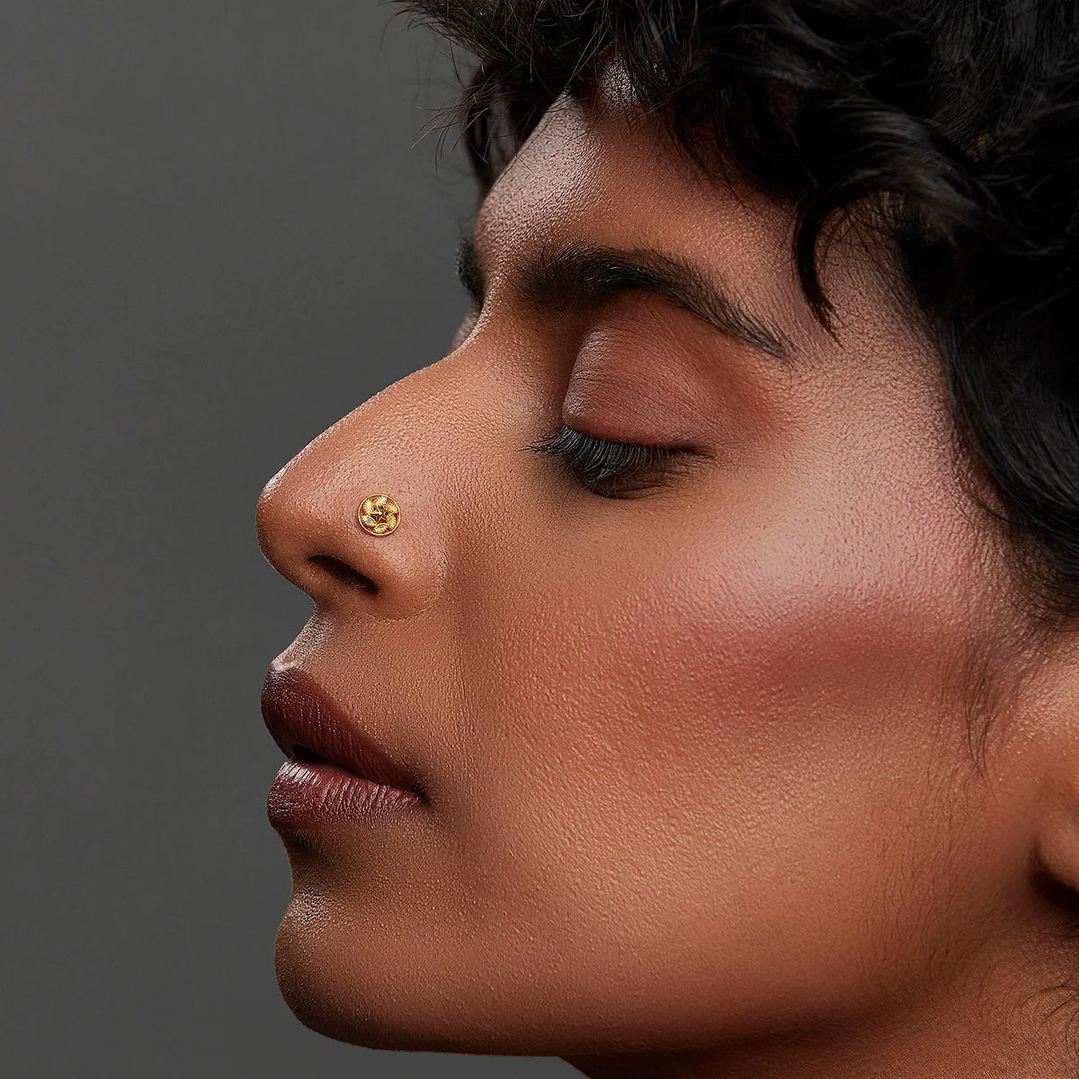 Side profile lifestyle shot of a woman wearing a round 18K gold nose pin on her nose