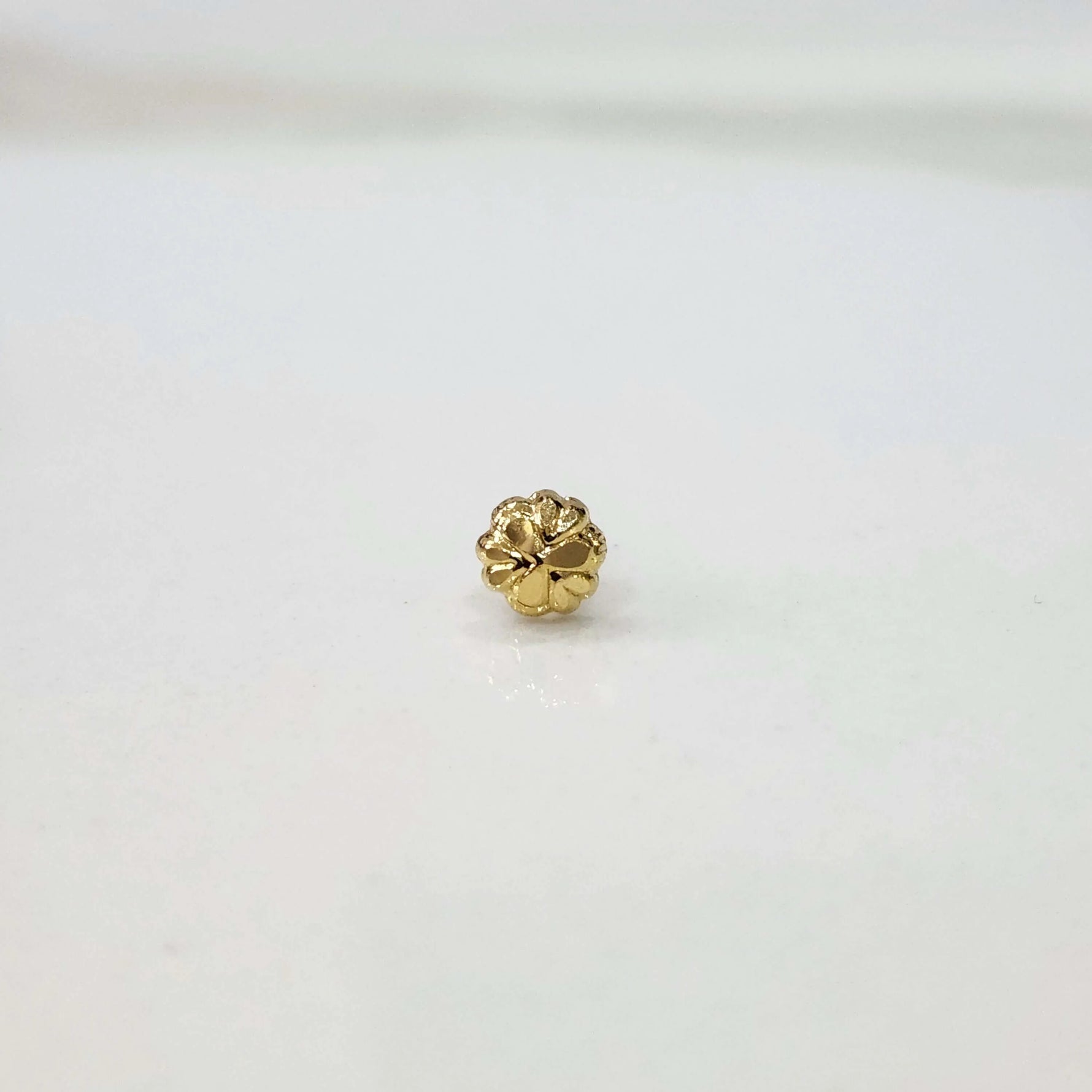 Front view of a small gold nose pin on a white background showcasing fine detailing and compact size