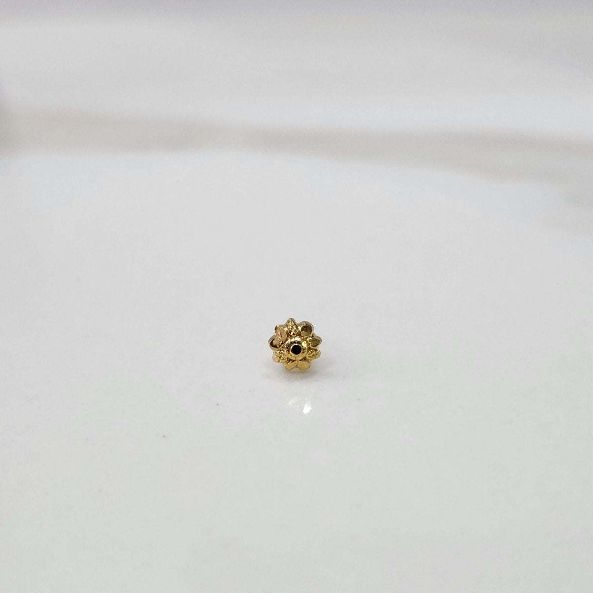 Front view of a small floral gold nose pin placed on a clean white background showing its delicate design and compact size