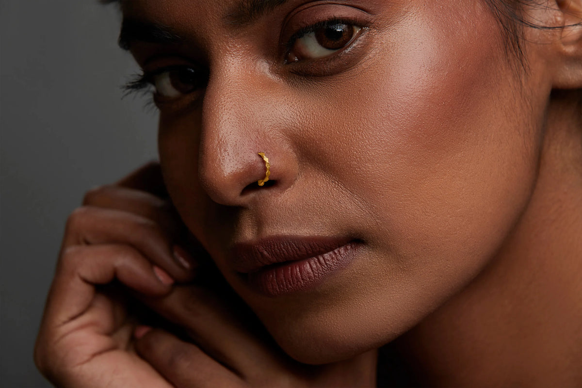 Woman wearing a minimal zigzag 18K gold nose ring styled for everyday elegance against a neutral backdrop