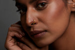 Woman wearing a minimal zigzag 18K gold nose ring styled for everyday elegance against a neutral backdrop