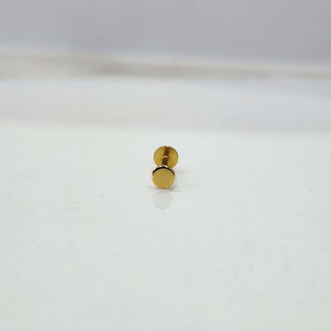 Close-up of tiny round gold nose pin placed on white surface showing clean detailing