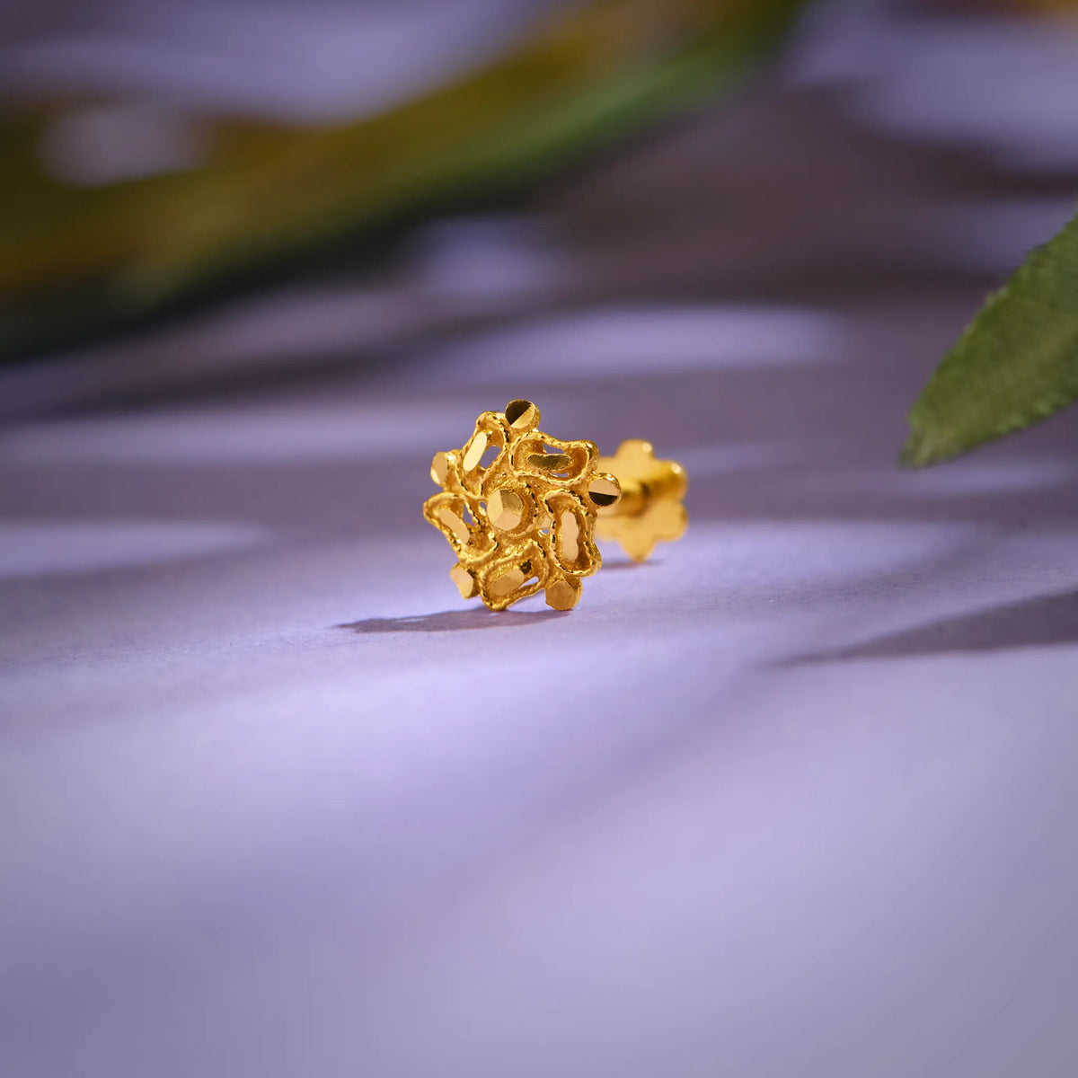 Close up of an intricate floral 18K nose pin gold placed on a soft pastel background highlighting detailed craftsmanship