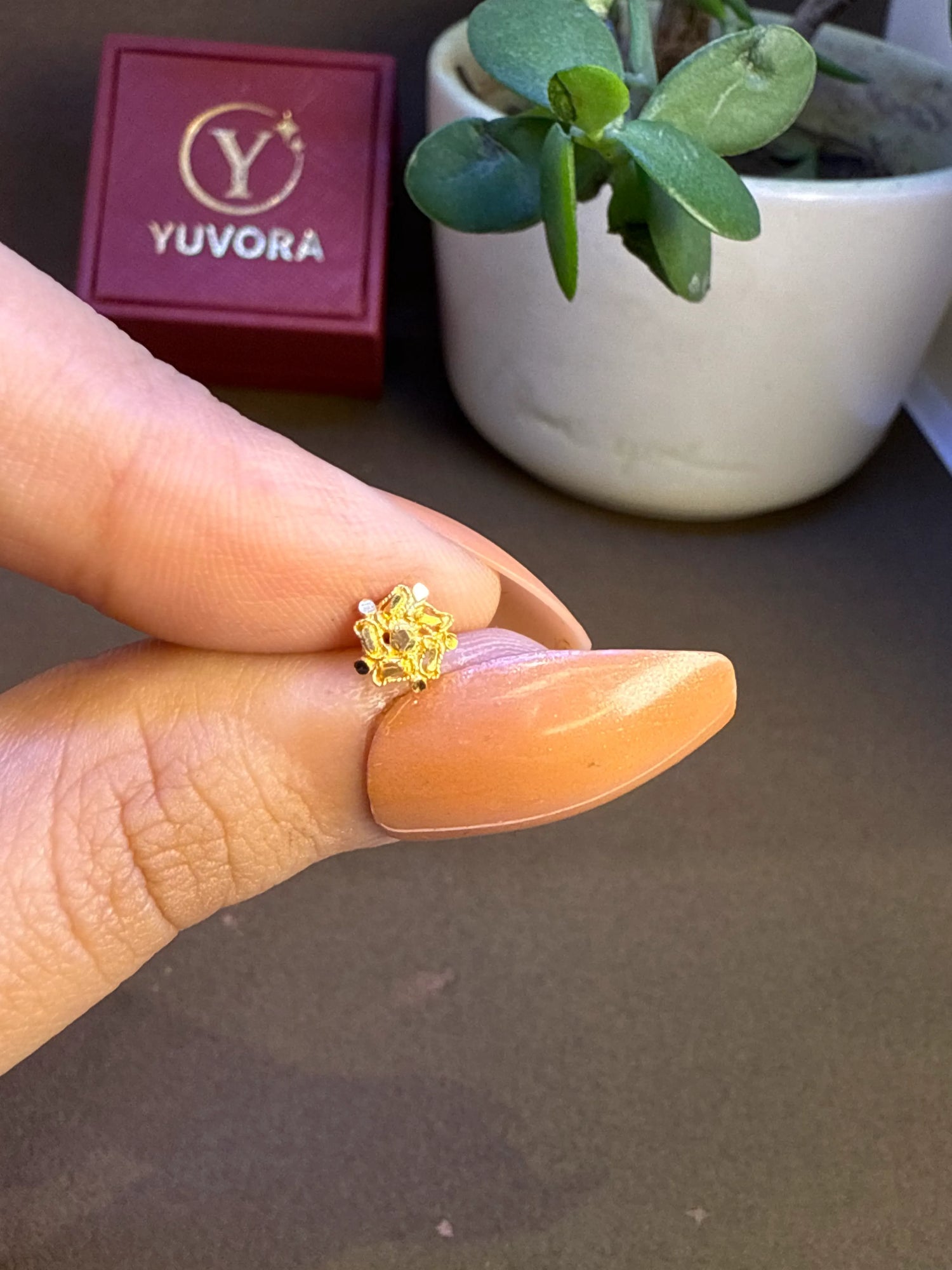 Hand holding a small floral 18K nose pin gold near a jewellery box to show its lightweight and wearable size