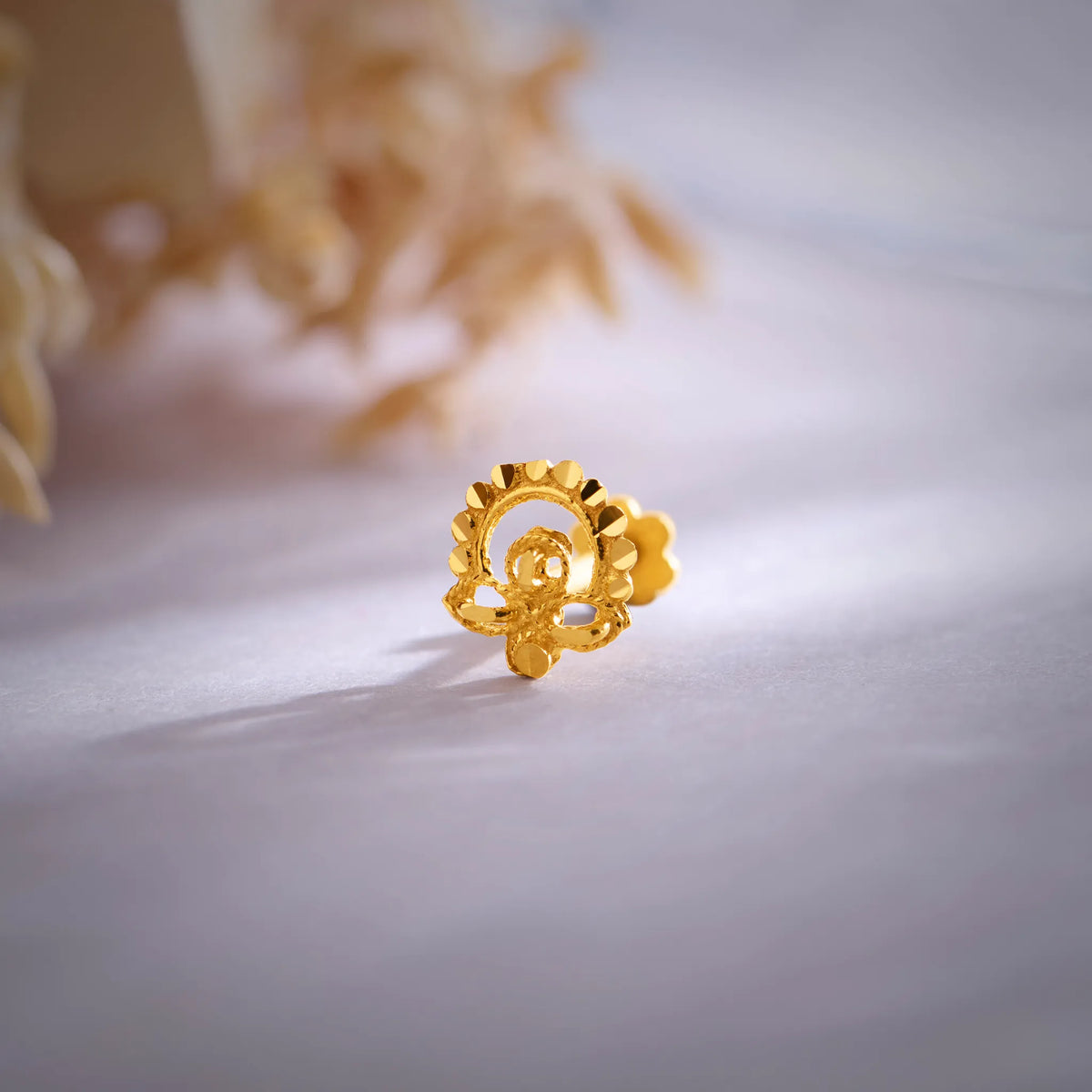 Close up of a floral 18K nose pin gold placed on a soft white surface highlighting intricate craftsmanship and polished finish