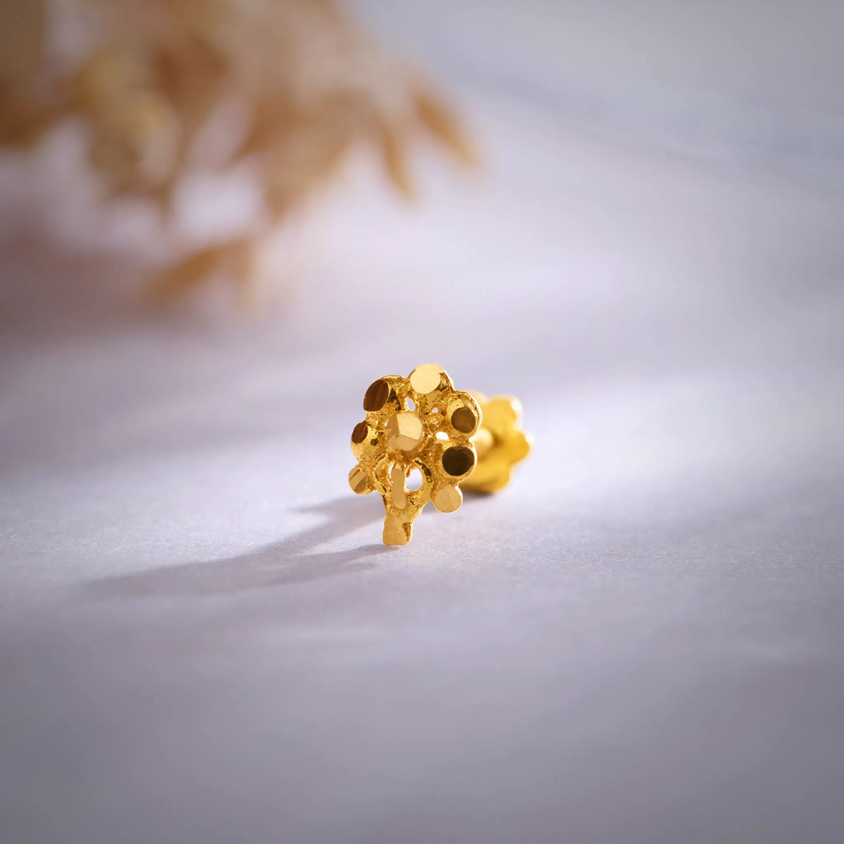 Front view close up of a floral 18K nose pin gold placed on a soft white surface highlighting intricate detailing and polished finish