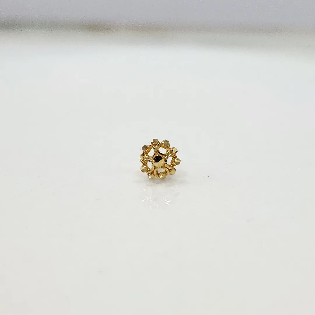 Close up front view of a floral inspired 18K gold nose pin placed on a clean white surface highlighting intricate petal detailing and compact size