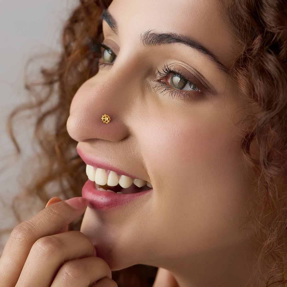Woman smiling while wearing a small floral 18K gold nose pin styled for elegant everyday wear
