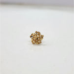 Close-up of the floral 18K gold nose pin on a smooth white surface displaying its polished finish