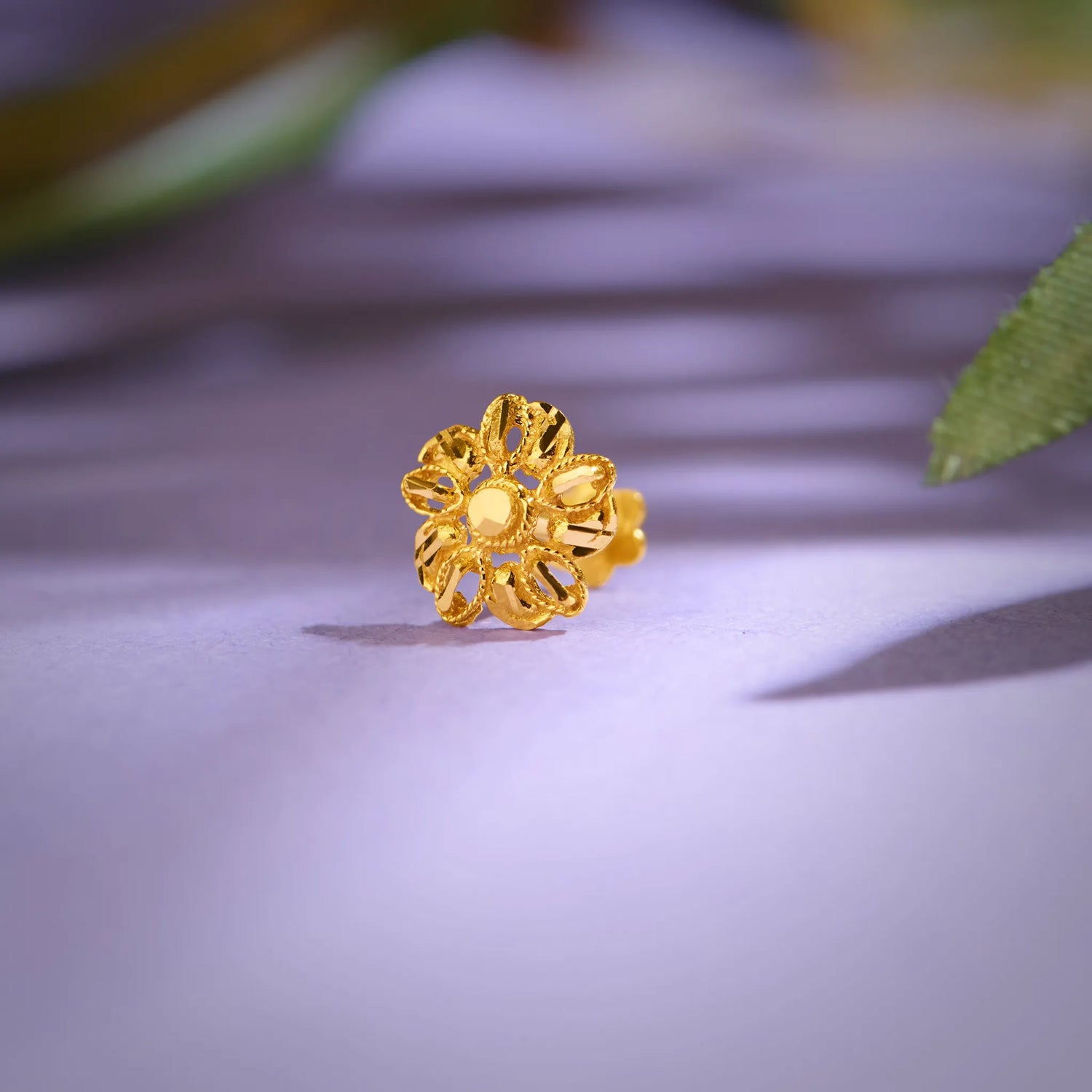 Close-up of a floral 18K gold nose pin placed on a soft purple surface highlighting its intricate handcrafted detailing