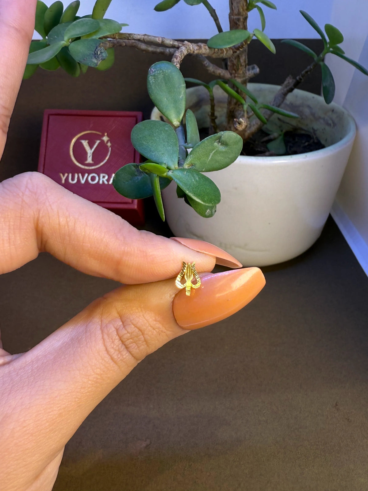 Hand holding a tiny 18K gold twisted nose pin near a Yuvora box highlighting its compact size and fine craftsmanship
