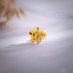 Close up of a floral 18K nose pin gold placed on a soft white surface highlighting detailed craftsmanship and polished finish