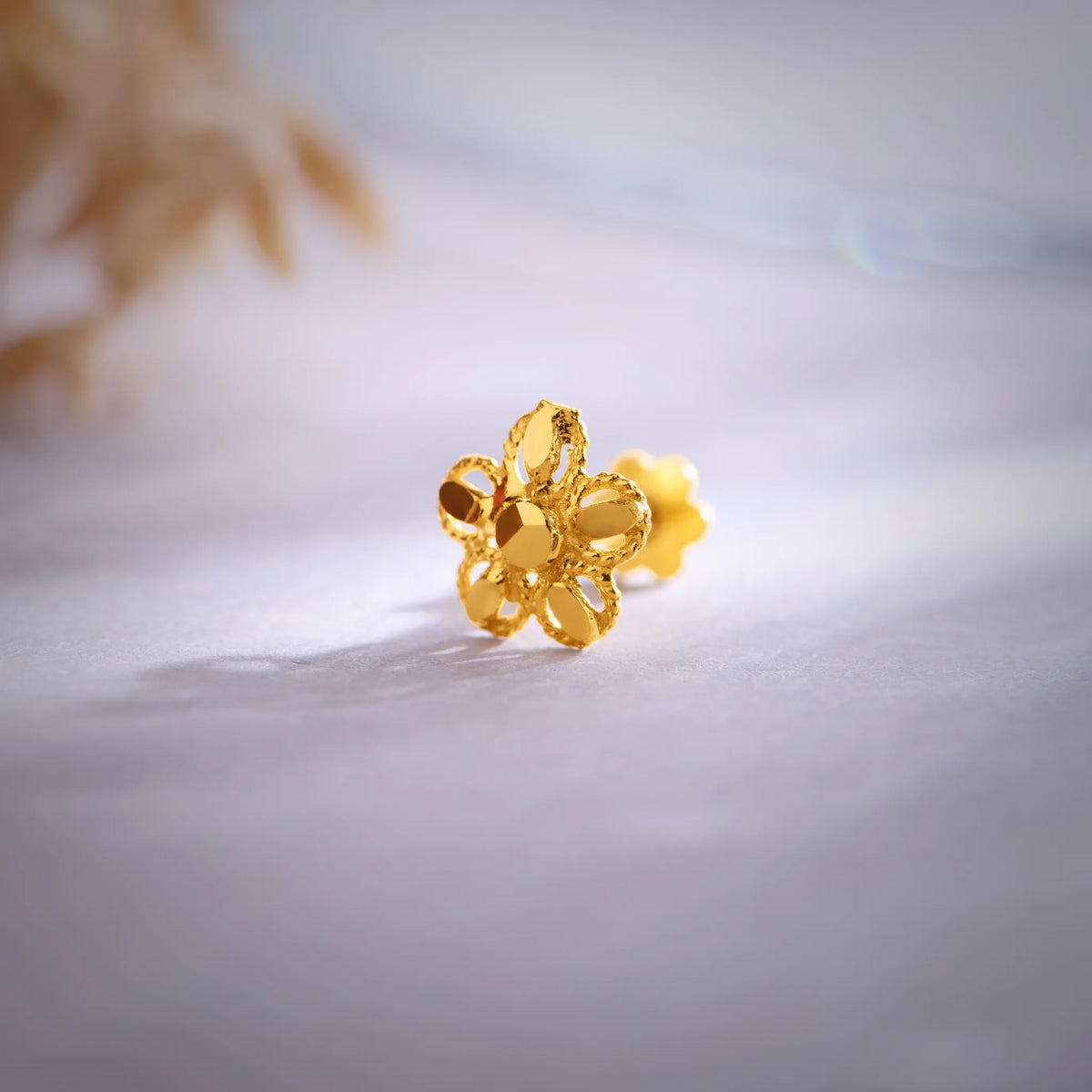 Close up of a floral 18K nose pin gold placed on a soft white surface highlighting detailed craftsmanship and polished finish
