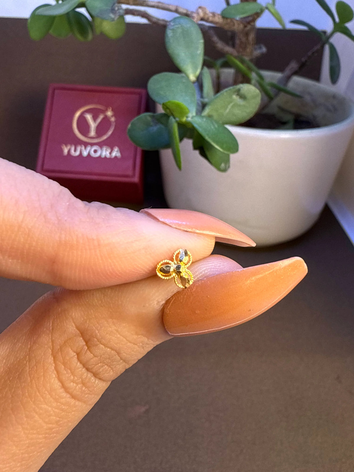 Hand holding a small 18K nose pin gold near a jewellery box showing lightweight design and wearable size