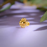 Close up of an ornate floral 18K nose pin gold placed on a soft purple surface highlighting intricate craftsmanship and polished shine