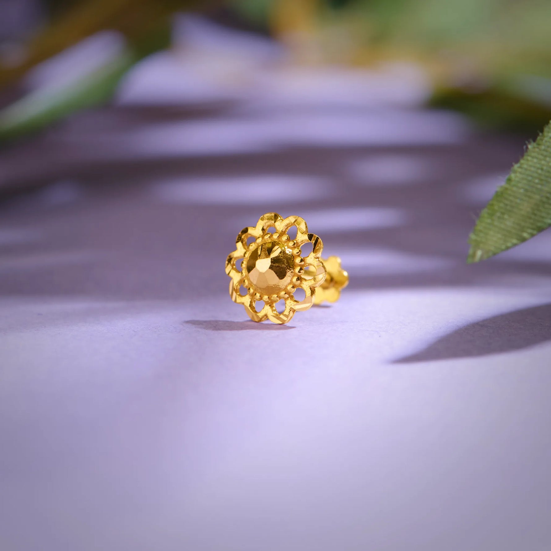 Close up of an ornate floral 18K nose pin gold placed on a soft purple surface highlighting intricate craftsmanship and polished shine