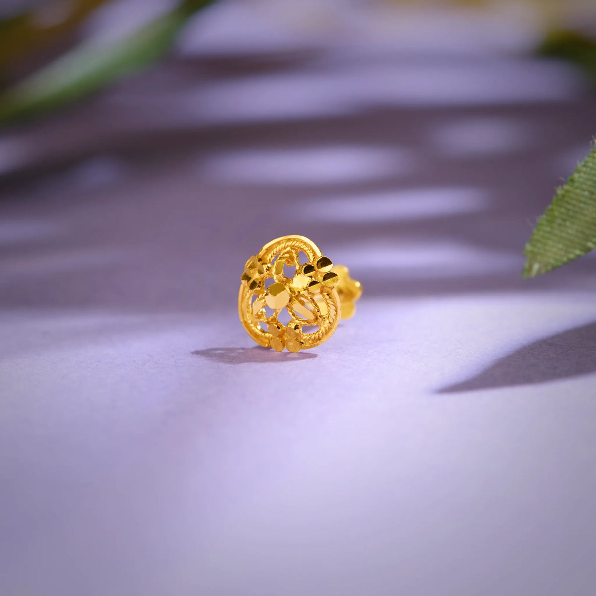 Close-up of an ornate floral 18K nose pin gold placed on a soft pastel surface highlighting its intricate openwork design