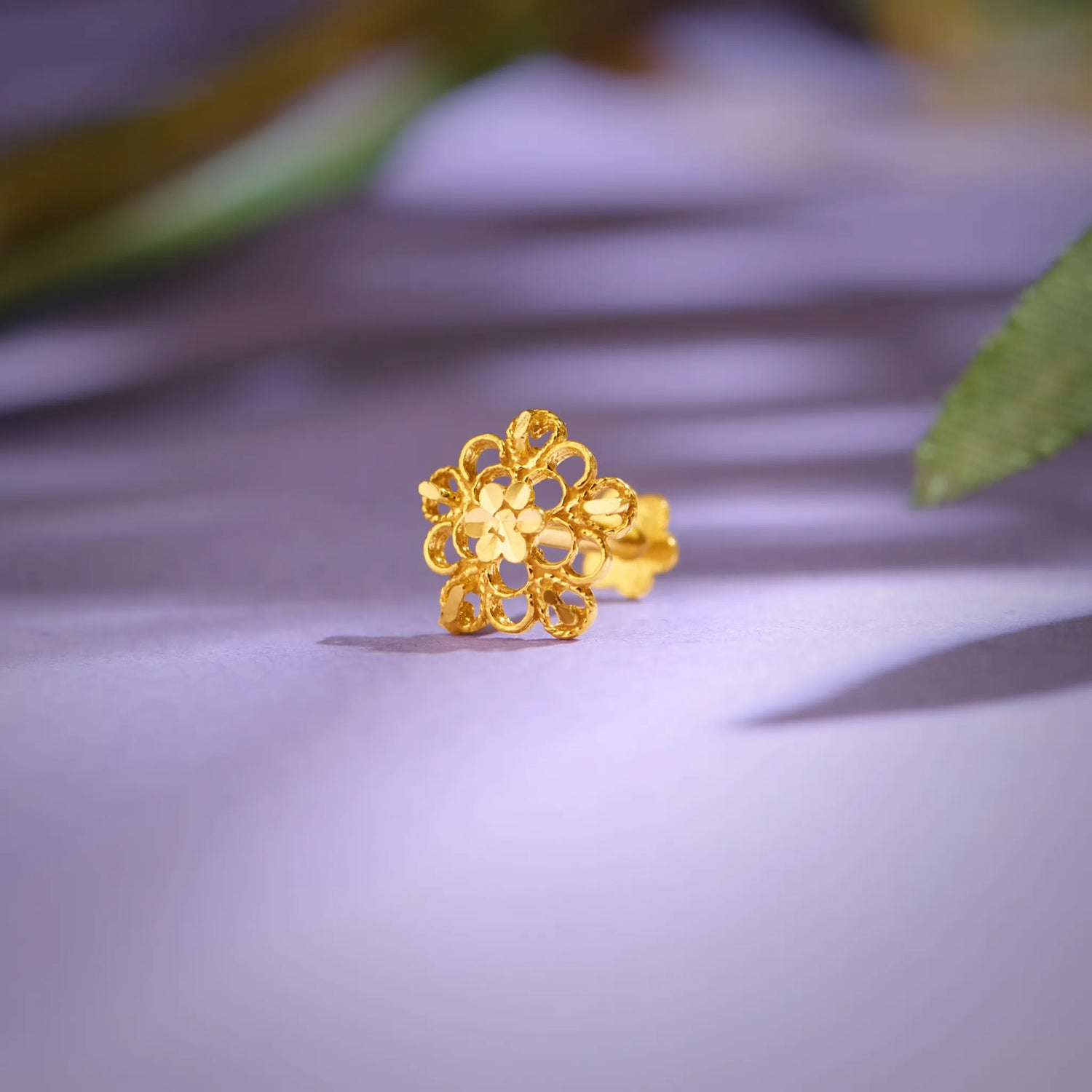 Close-up of floral 18K nose pin gold placed on a soft lavender surface highlighting its intricate handcrafted design
