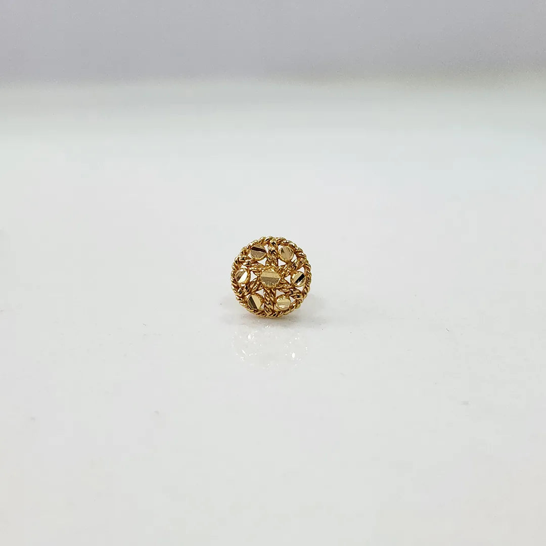 Front angle view of the round floral 18K gold nose pin placed on a white surface emphasizing its compact size