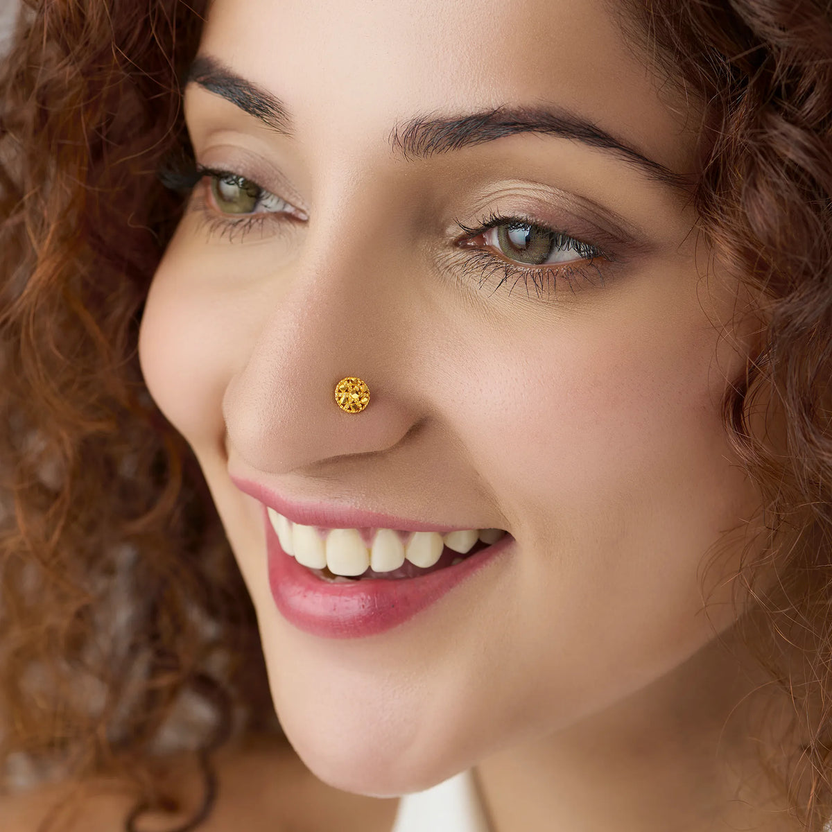 Woman smiling while wearing a small round floral 18K gold nose pin showcasing elegant everyday styling