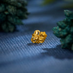 Close-up of a handcrafted 18K gold nose pin placed on a textured blue surface surrounded by soft greenery