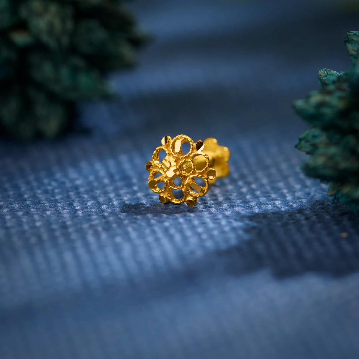 Close-up of an intricately crafted 18K gold floral nose pin placed on a textured blue surface highlighting its detailed design