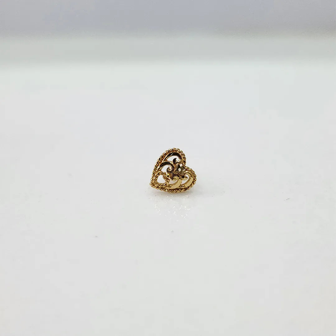 Side view of 18K heart motif gold nose pin placed on a white surface reflecting its polished finish