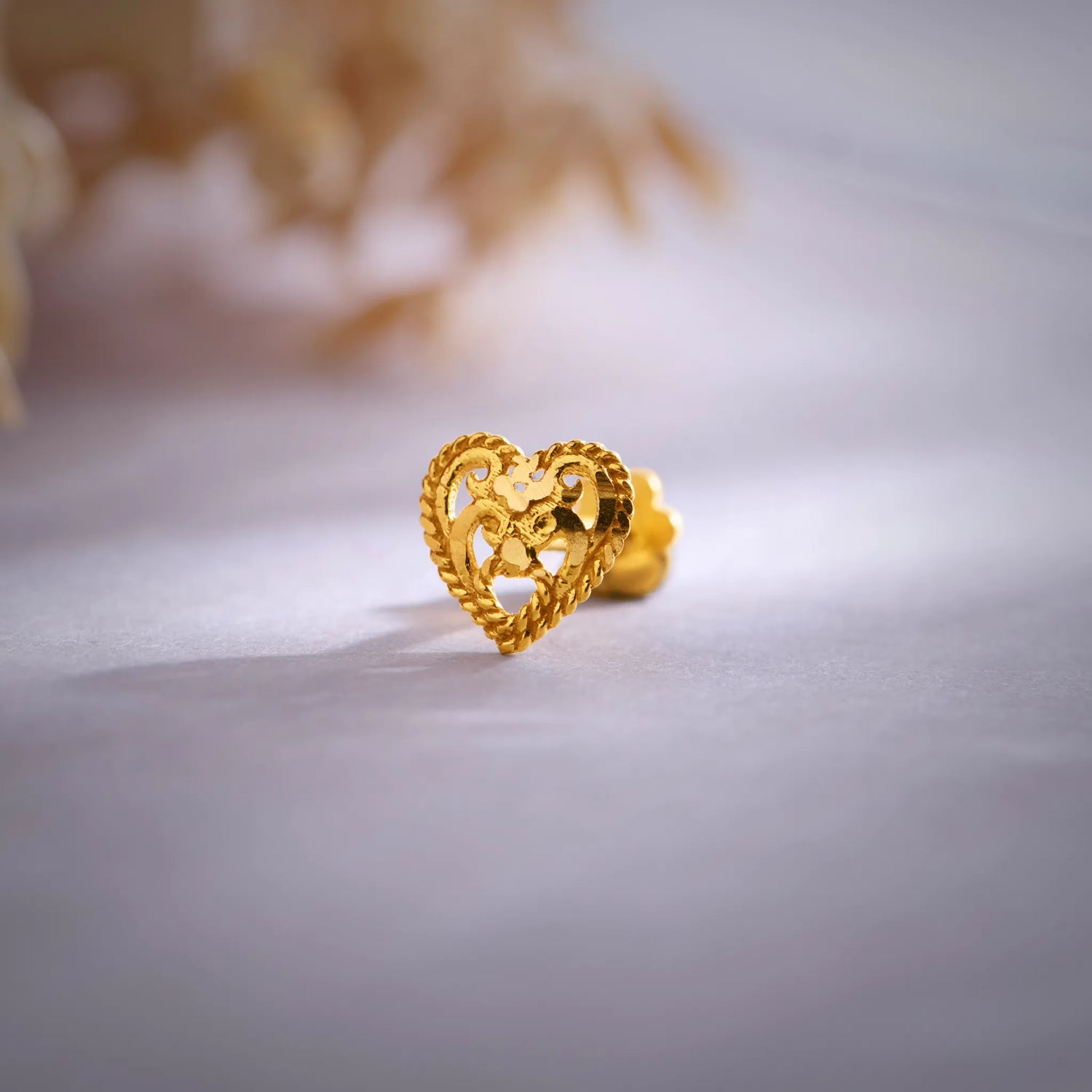 Close-up of an 18K heart-shaped gold nose pin placed on a soft surface showcasing its delicate cutwork design