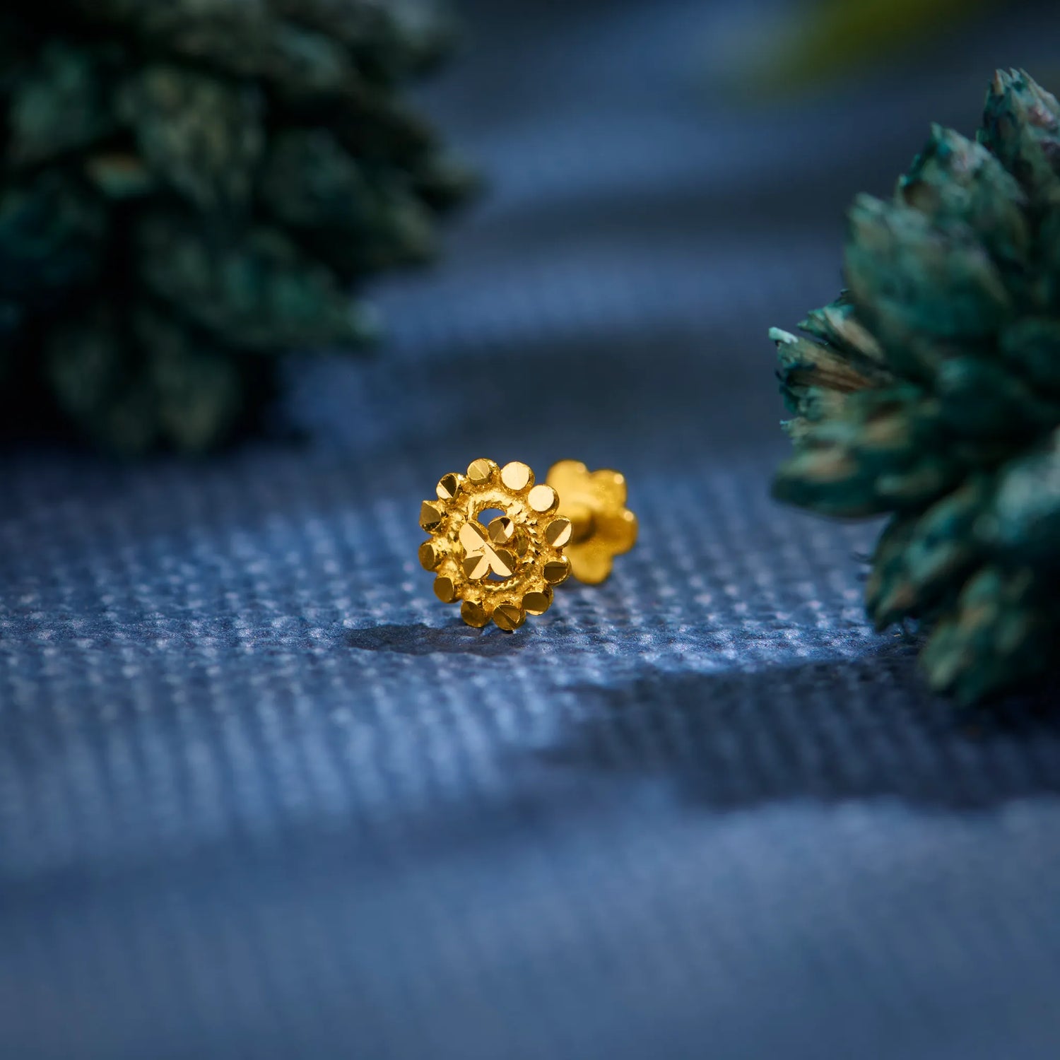 Close-up of an 18K floral gold nose pin placed on a textured blue surface highlighting its intricate detailing