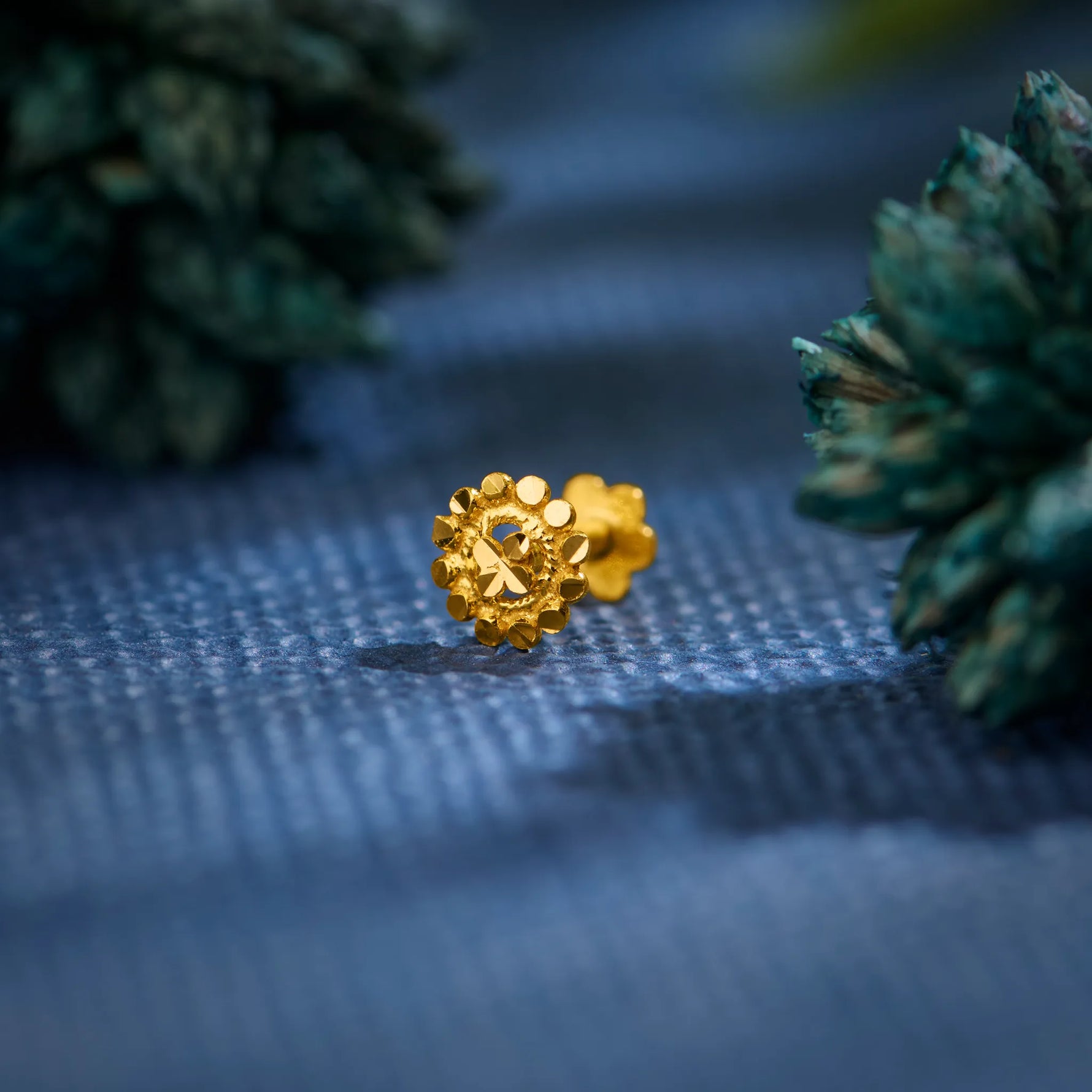 Close-up of an 18K floral gold nose pin placed on a textured blue surface highlighting its intricate detailing