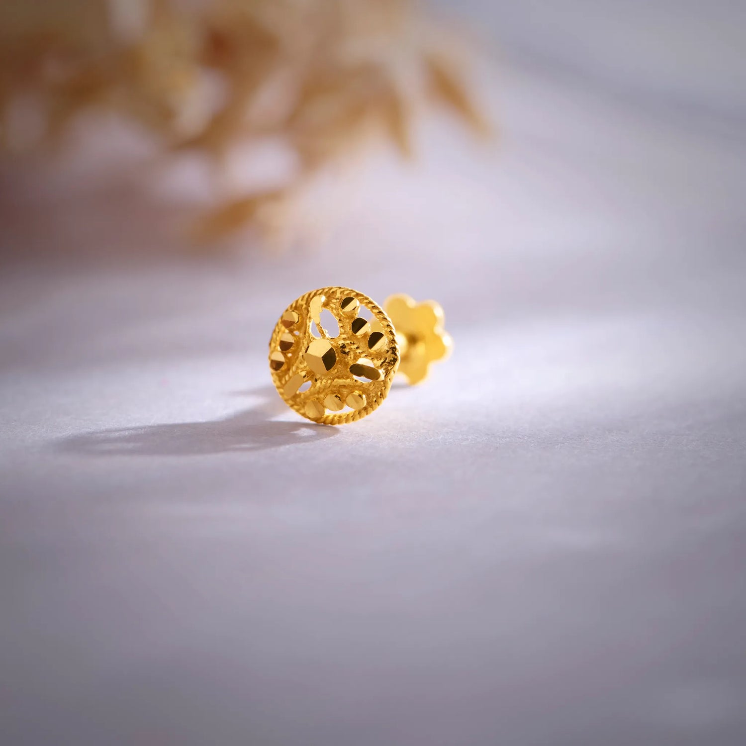 Close-up of an intricate 18K floral gold nose pin placed on a soft surface showcasing its detailed craftsmanship