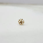 Side view of a delicate 18K gold floral nose pin placed on a white surface displaying its polished finish
