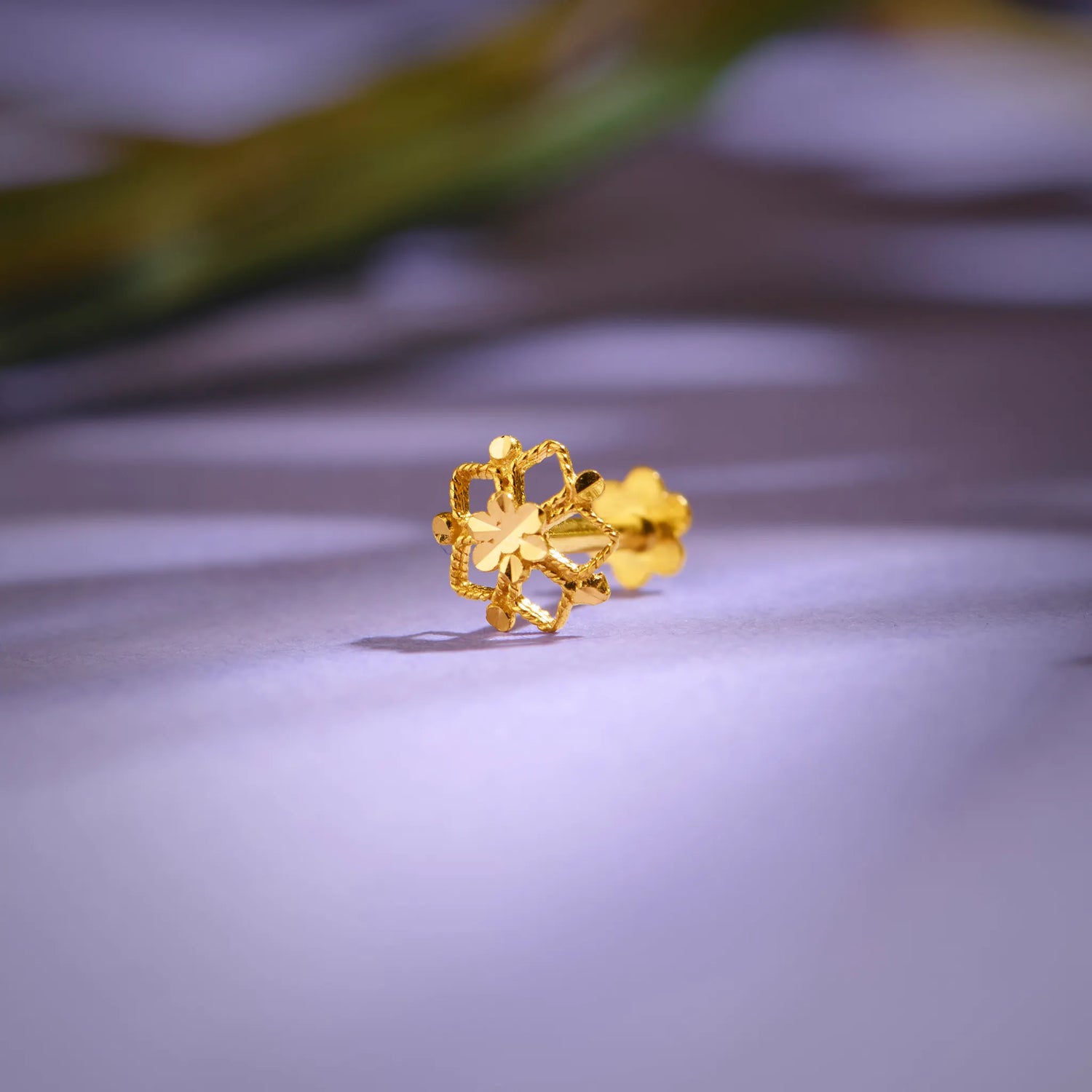 Close-up of a handcrafted 18K gold floral nose pin placed on a soft lavender surface highlighting its intricate detailing