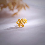 Close up of a floral 18K nose pin gold placed on a soft white surface highlighting intricate design and polished finish
