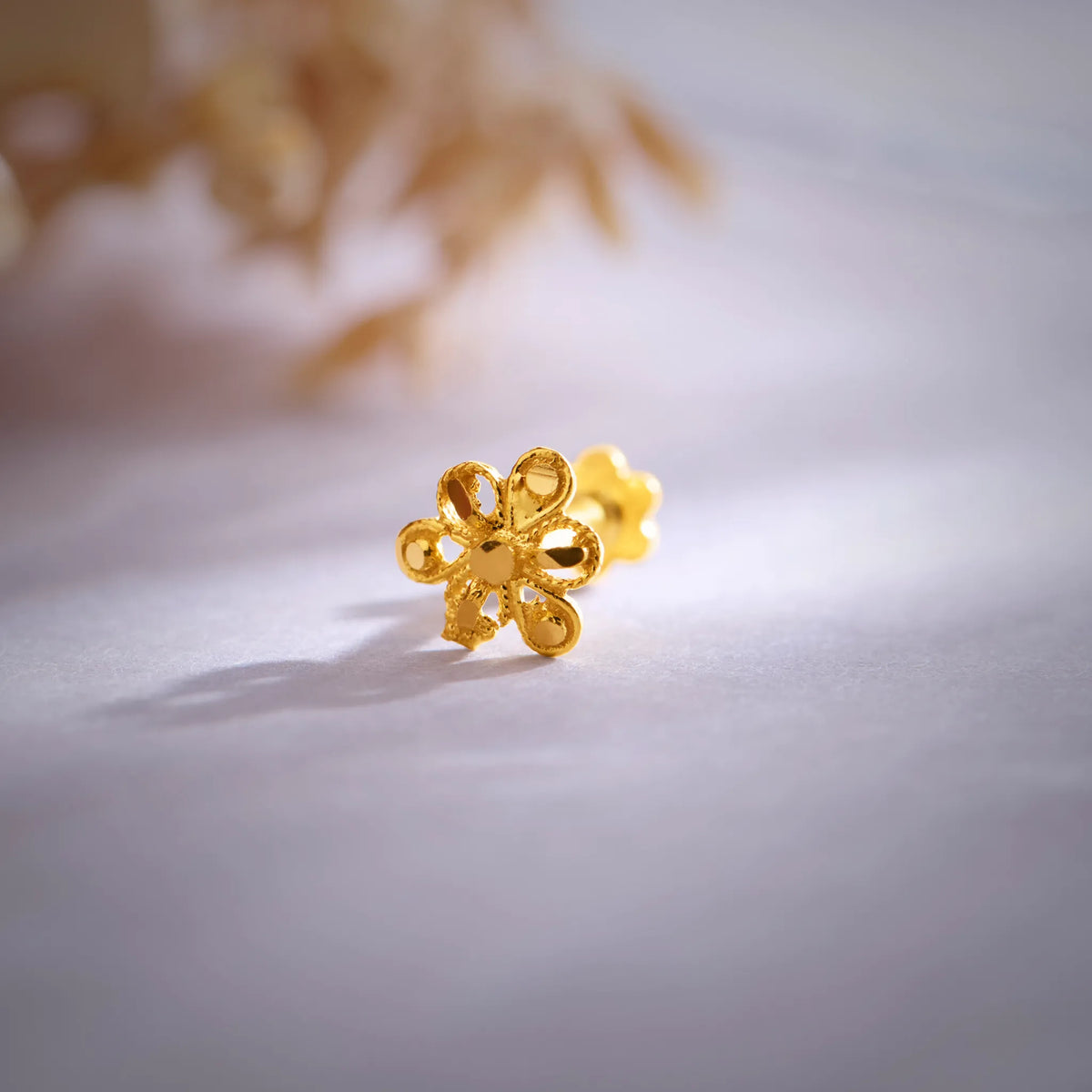 Close up of a floral 18K nose pin gold placed on a soft white surface highlighting intricate design and polished finish