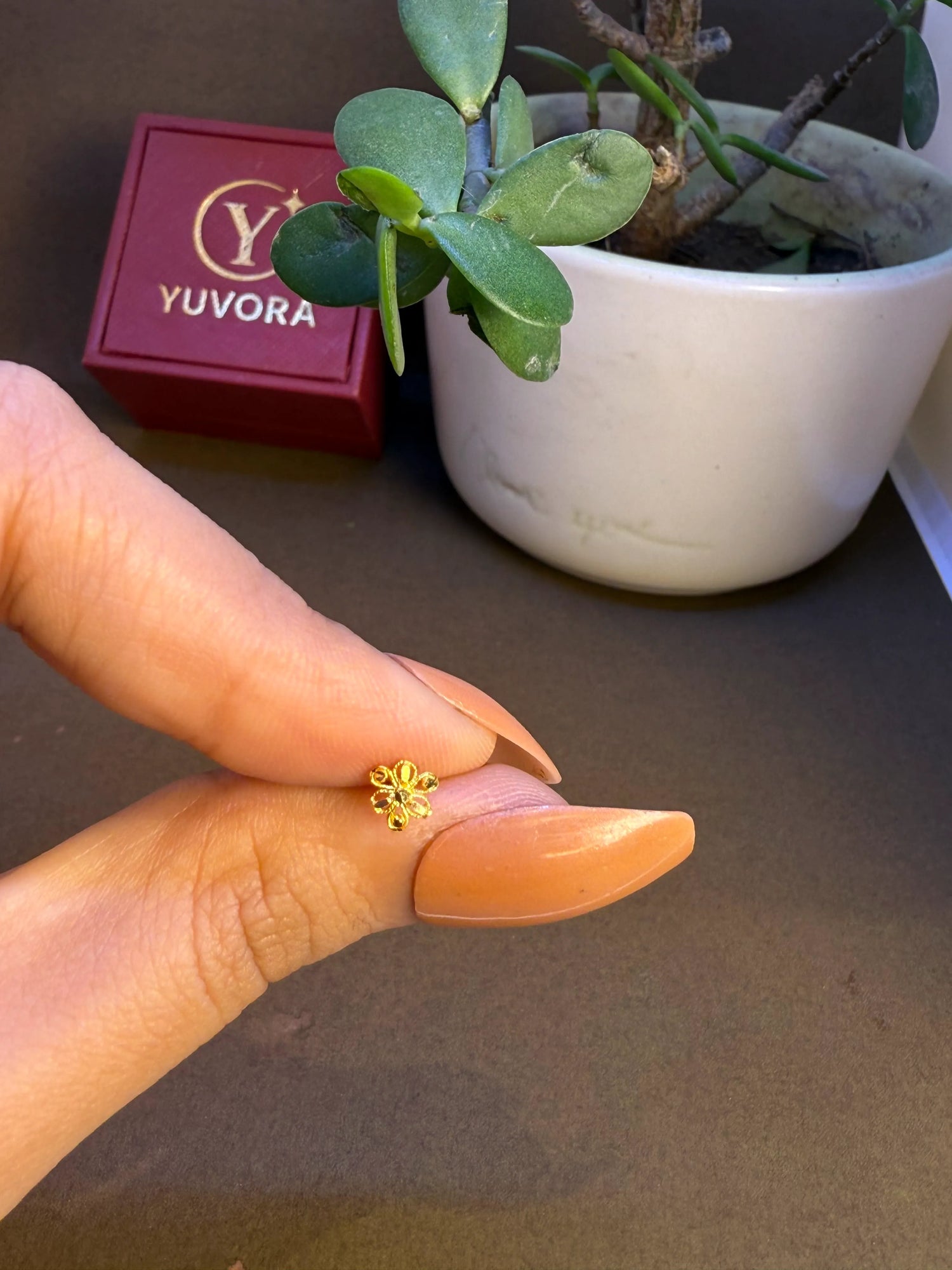Hand holding a tiny 18K nose pin gold near a jewellery box showing its lightweight feel and small wearable size