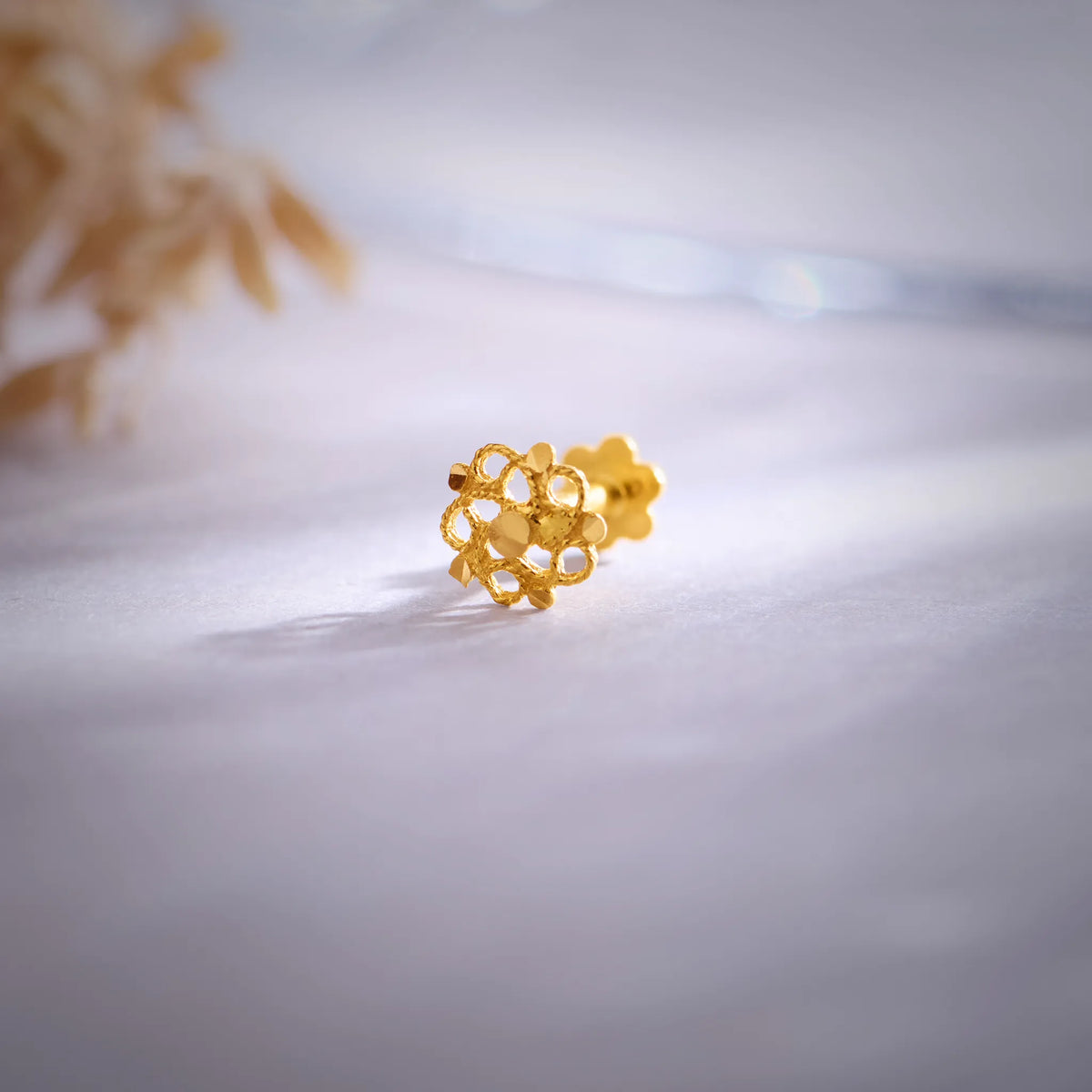 Close up of a floral 18K nose pin gold placed on a soft white surface highlighting its intricate openwork design