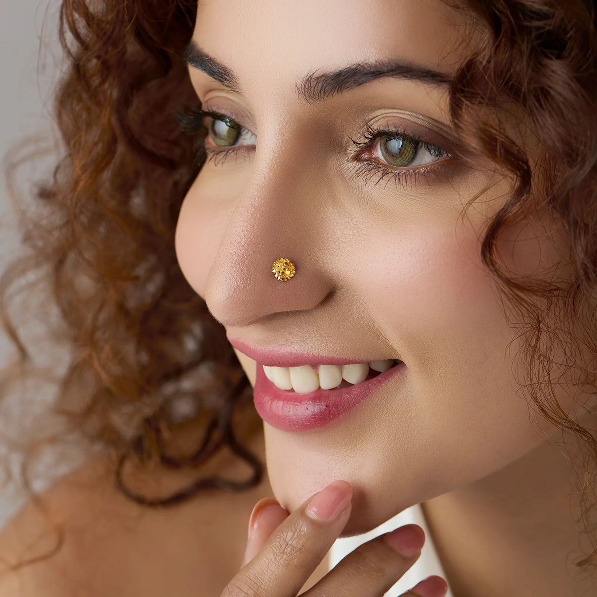 Woman with curly hair smiling while wearing a small round floral 18K gold nose pin for everyday elegance
