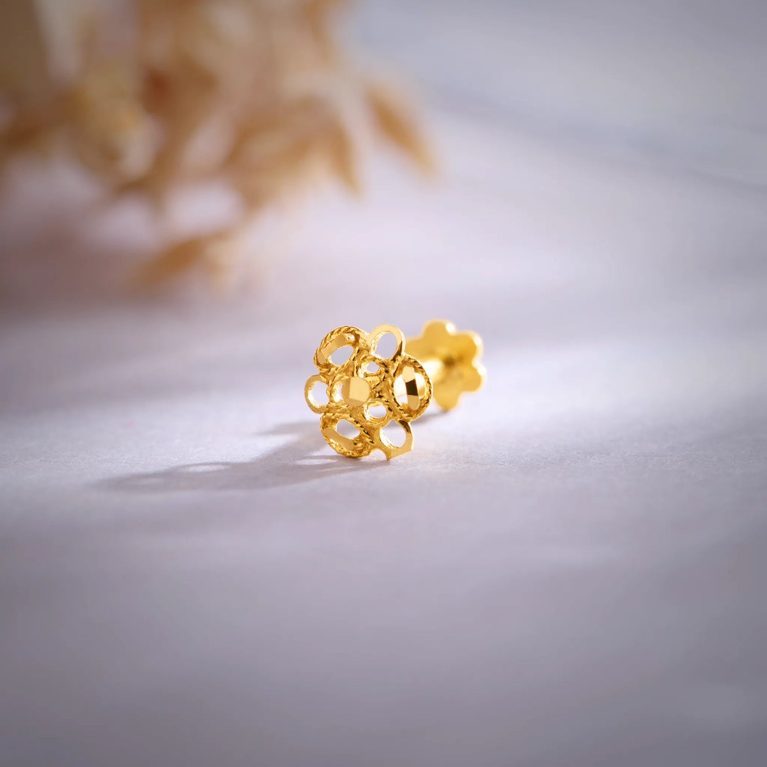 Close-up of floral 18K gold nose pin placed on a soft surface highlighting its intricate cutwork design
