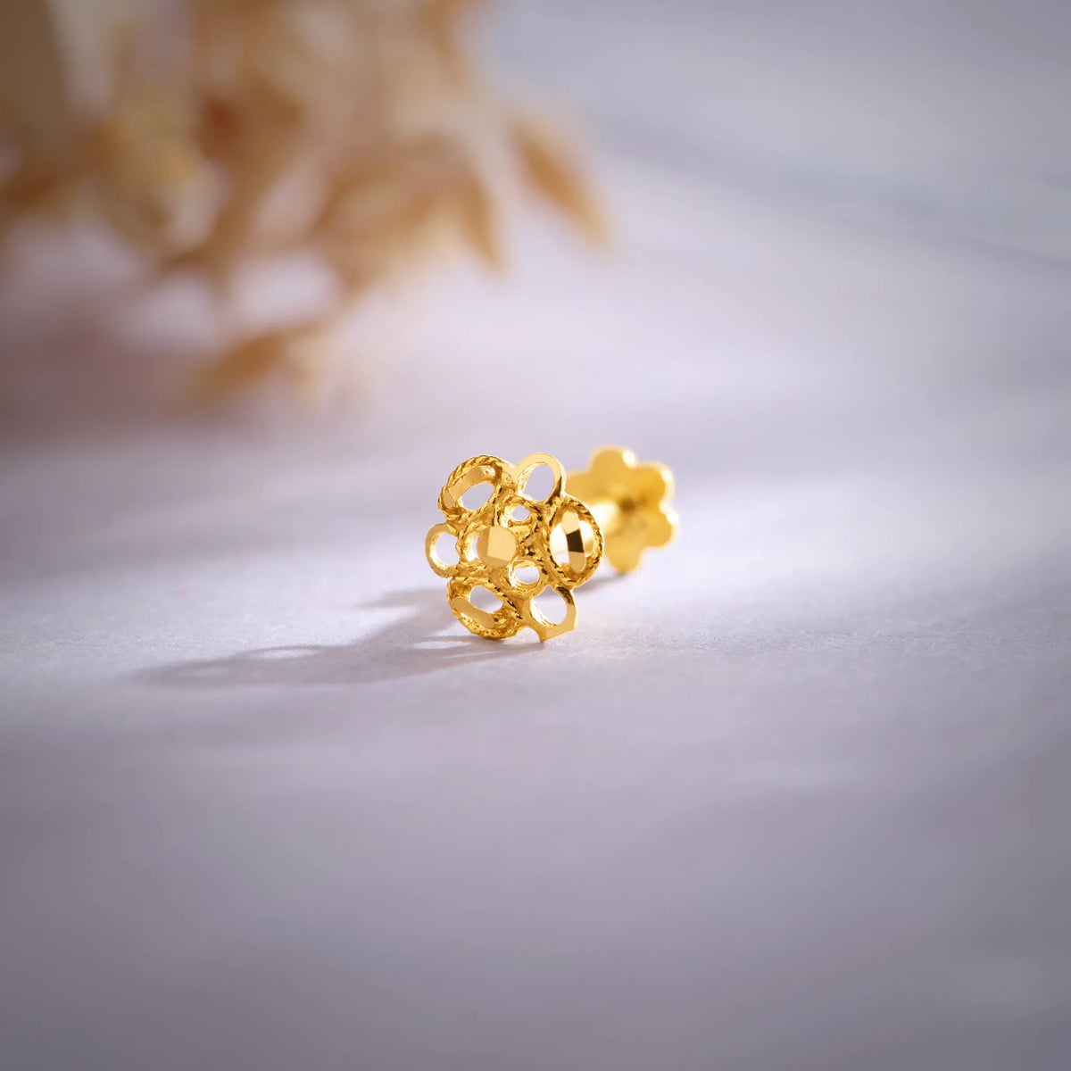 Close-up of floral 18K gold nose pin placed on a soft surface highlighting its intricate cutwork design