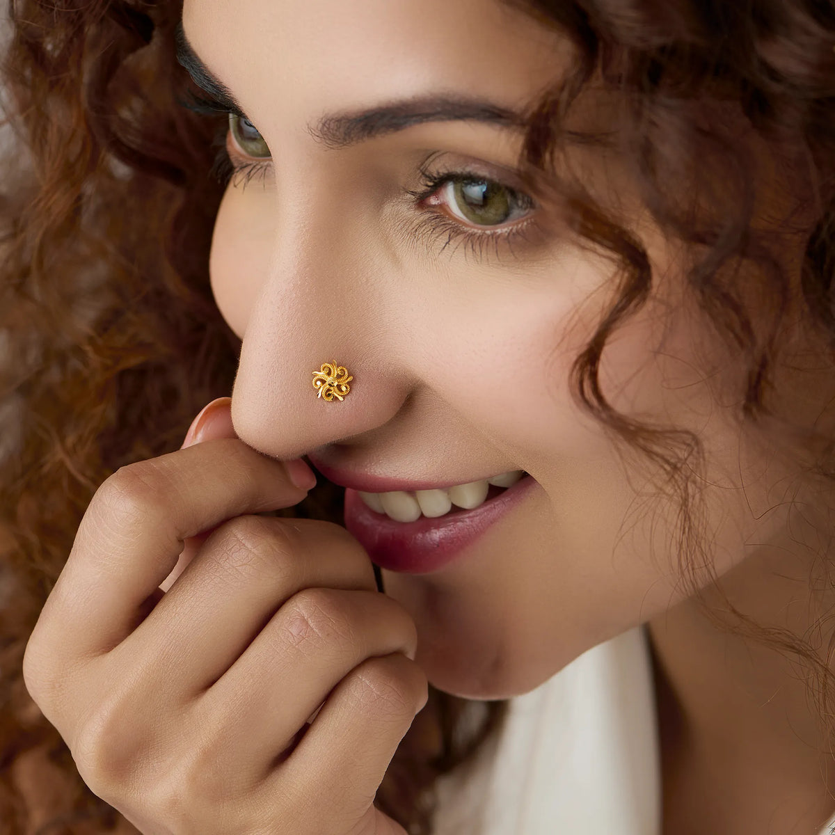 Woman wearing a small swirl design 18K gold nose pin smiling softly to highlight everyday elegance