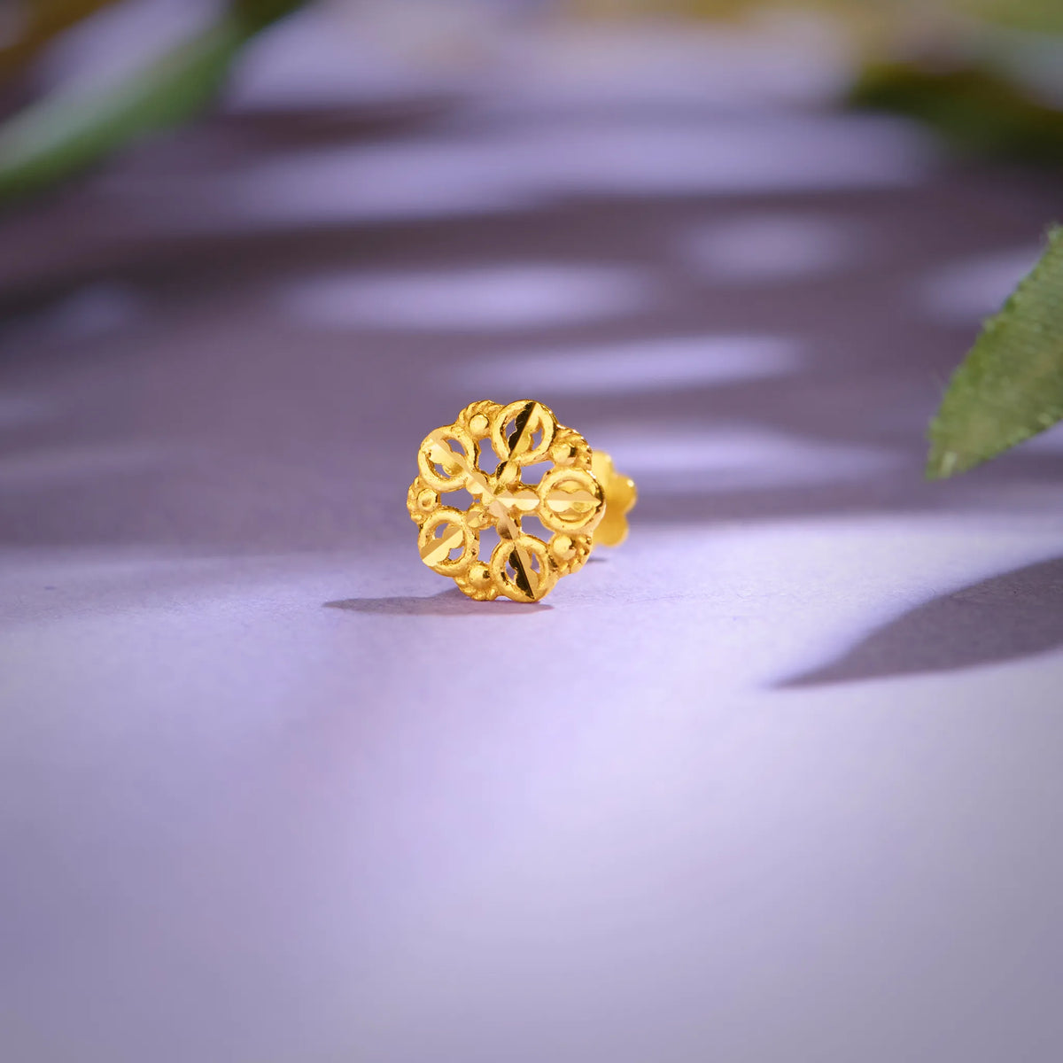 Close-up of floral patterned 18K nose pin gold placed on a soft purple surface highlighting its intricate openwork design