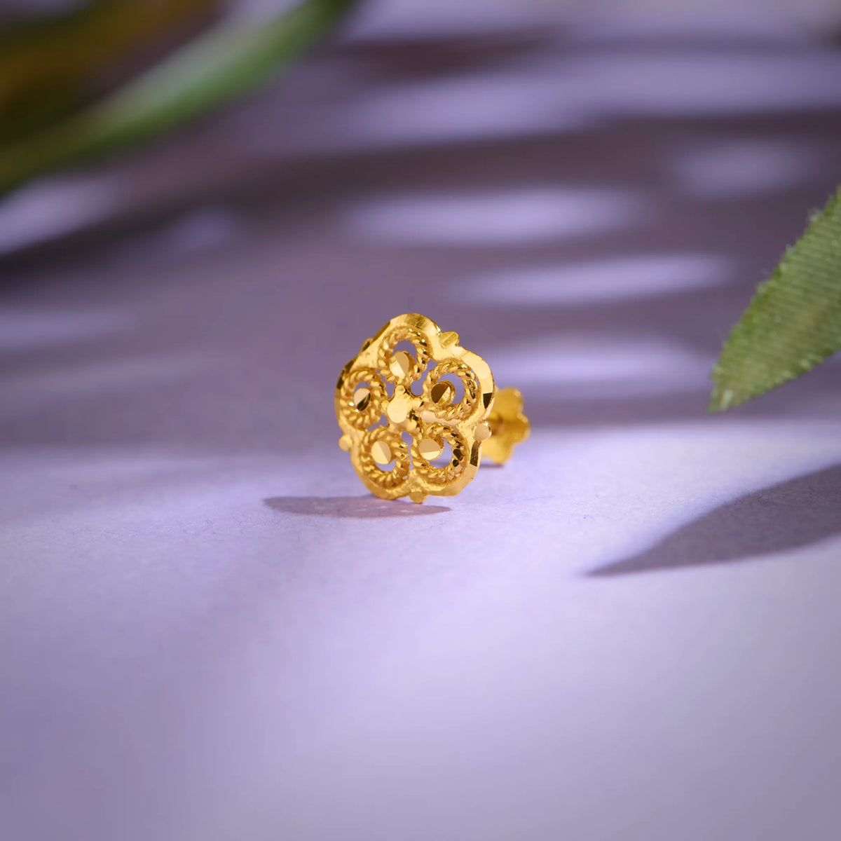 Close-up of floral 18K nose pin gold placed on a soft lavender surface highlighting its detailed craftsmanship