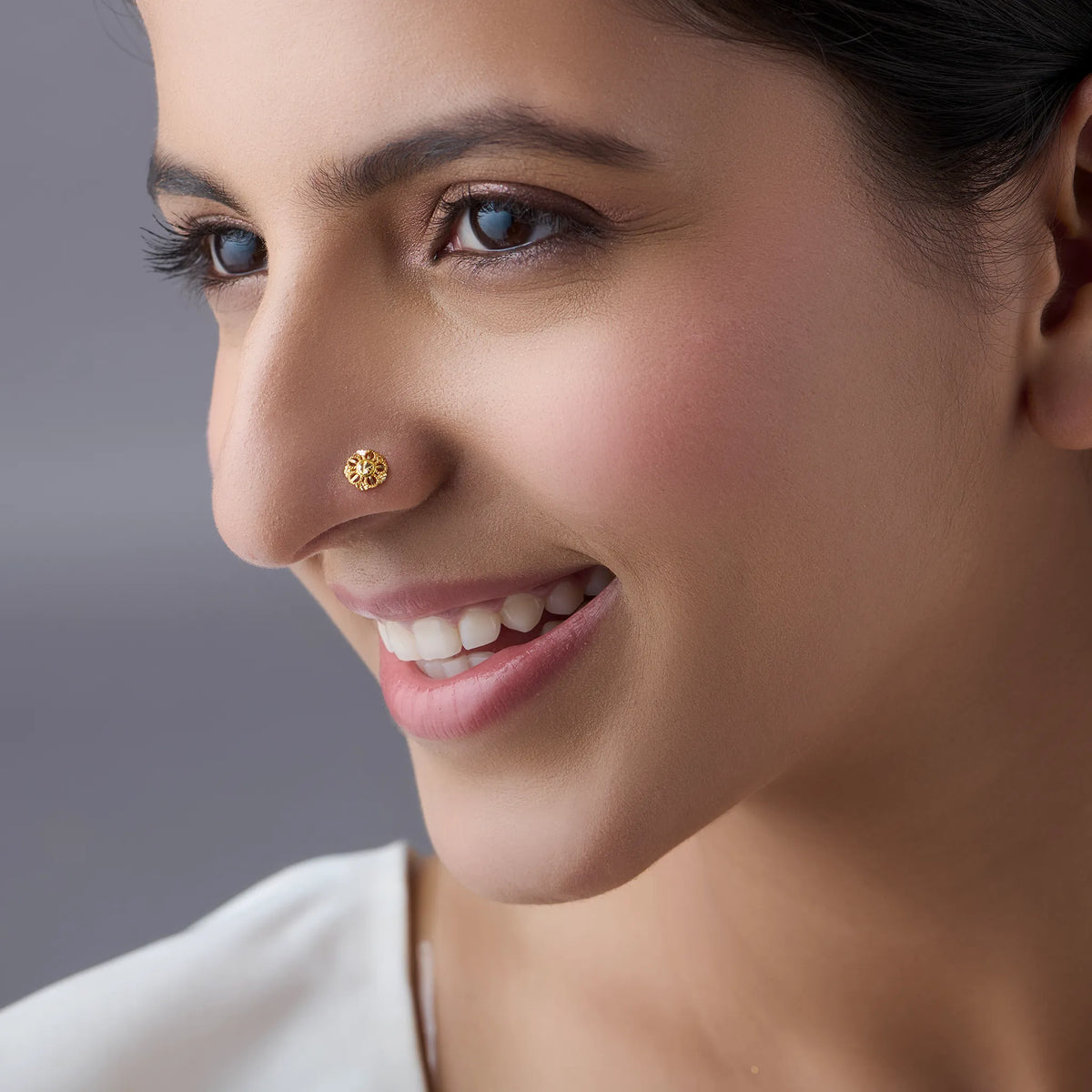 Woman smiling in a white outfit wearing a small floral design 18K gold nose pin for a minimal classy look