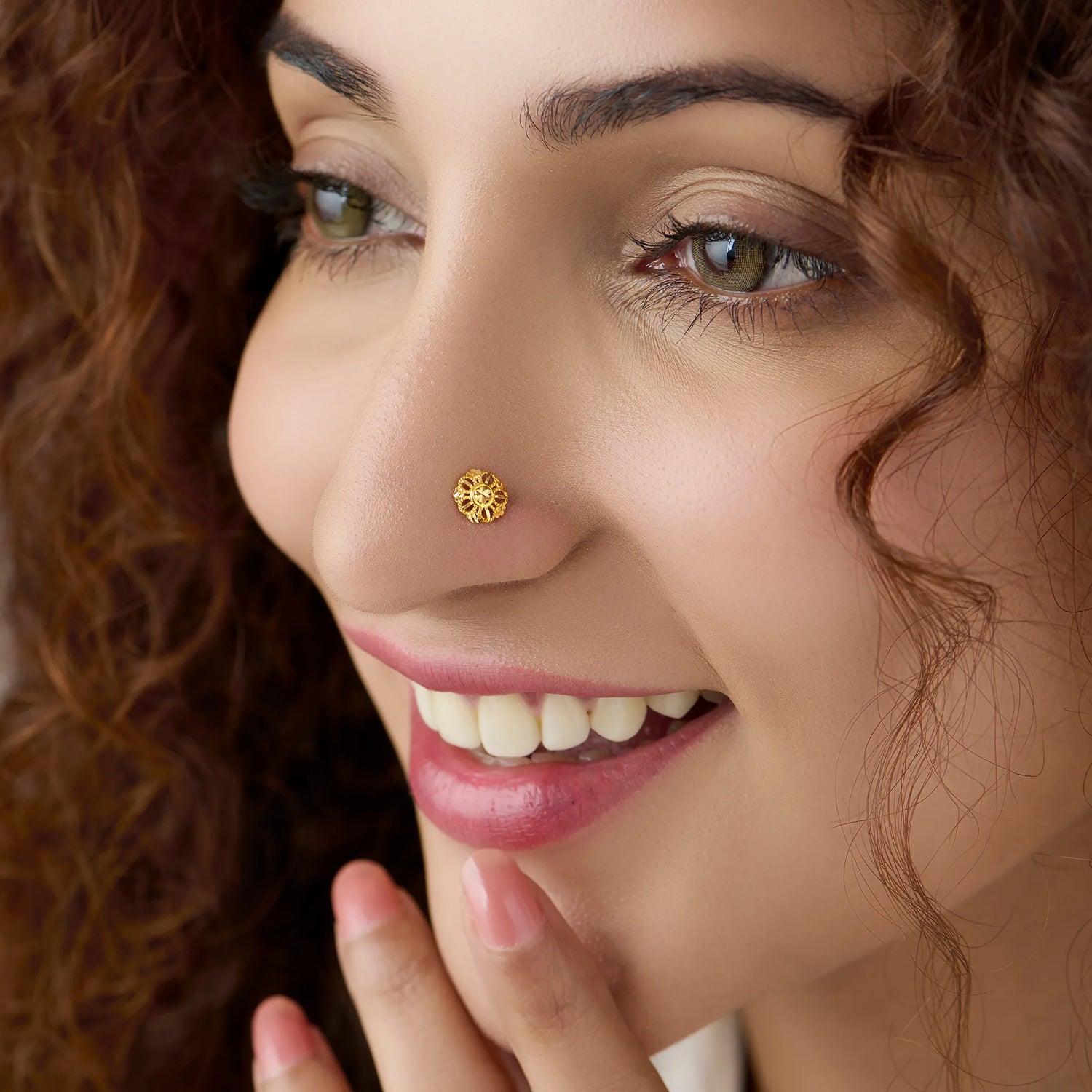 Woman with curly hair smiling while wearing a delicate floral 18K gold nose pin showing elegant everyday styling