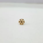 Side angle view of petite floral design gold nose pin on a white surface emphasizing its lightweight and minimal profile