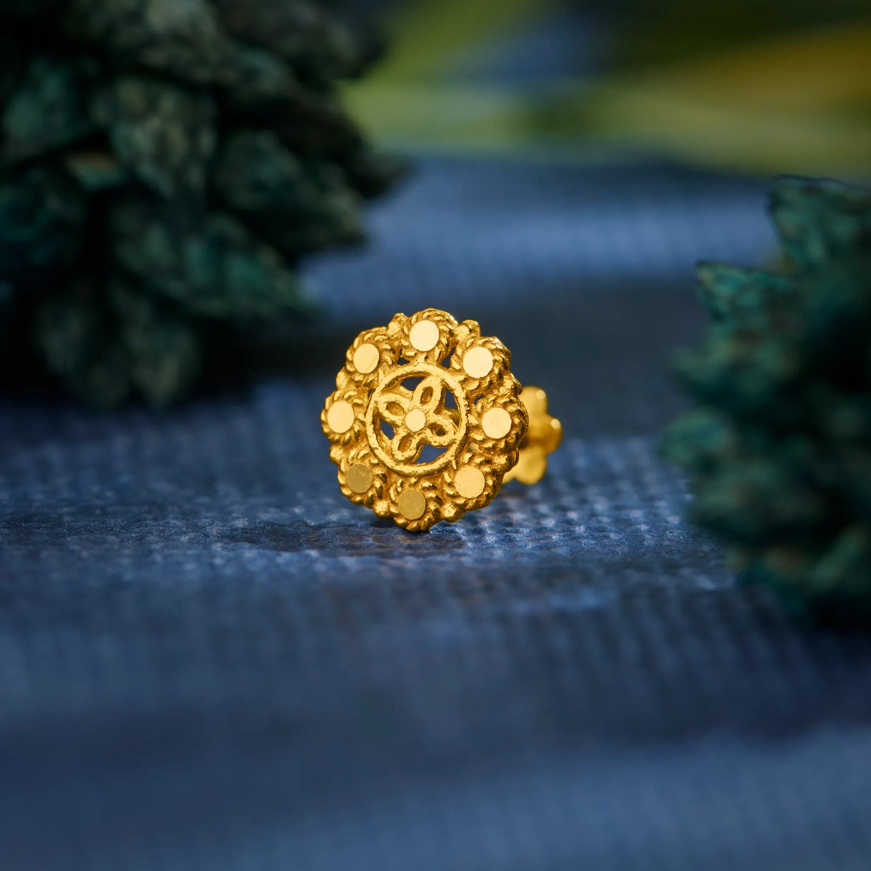 Close up of intricate floral gold nose pin placed on a textured blue surface highlighting detailed craftsmanship